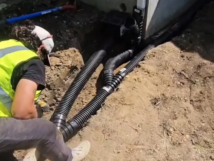 Crew member connecting downspouts to buried corrugated drain lines routed away from the foundation
